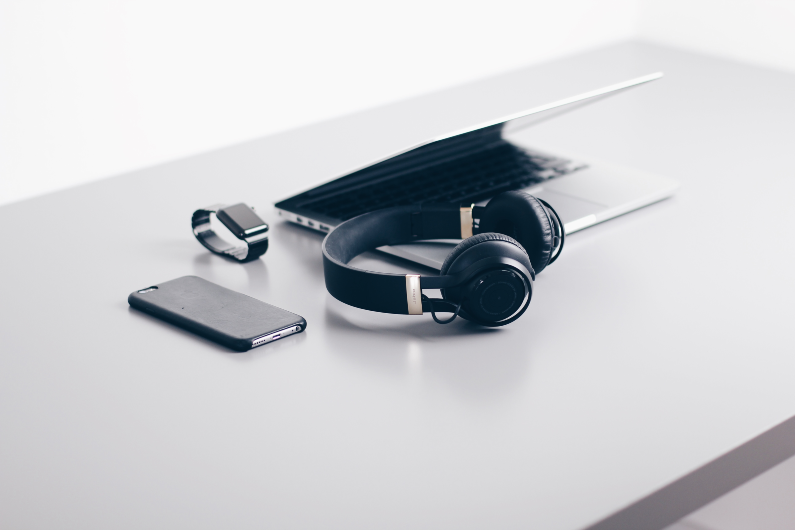 Desk with headphones, mobile phone, smart watch and laptop.
