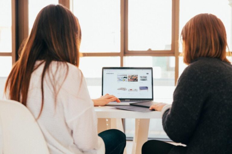 Two women engaged in discussion at a table, utilizing a laptop to explore an AI enterprise platform.